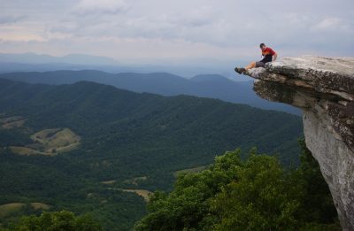 A student sitting on a rocky outcrop with views of the surrounding valley