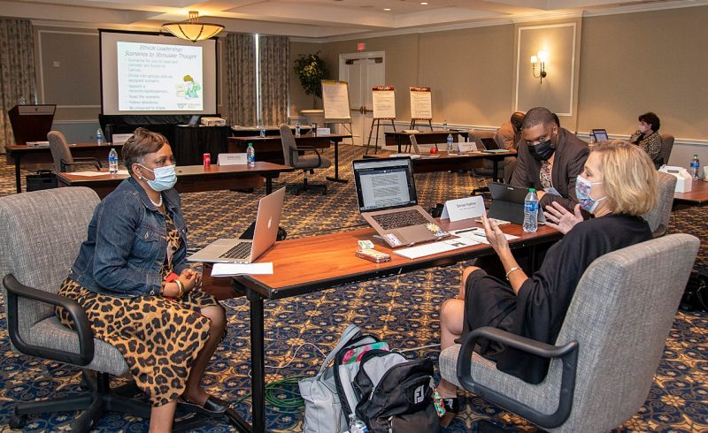 Three school administrators sit around the desk talking in a large conference room.