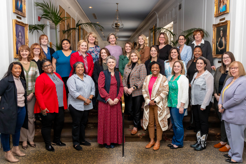 Group photo of inaugural cohort Outside group photo of about 25 women with dark woods in the background.